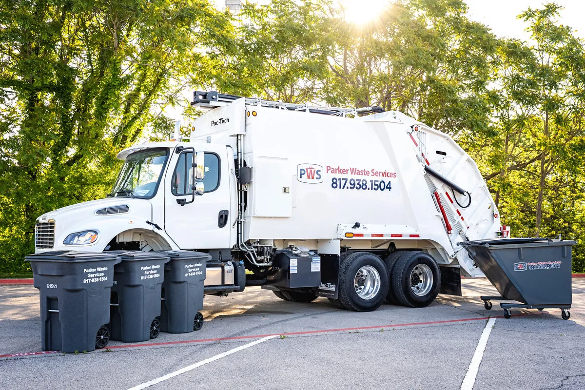 A rear-loading waste collection truck beside residential carts