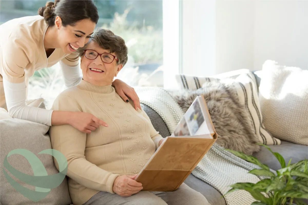 A caregiver and an older adult sitting together on a sofa at home